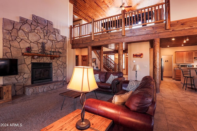 living room featuring a high ceiling, a stone fireplace, ceiling fan, and wood ceiling