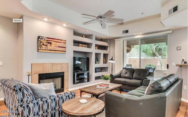 8245 E Bell Rd Unit 103, Scottsdale, AZ 85260 - living area featuring wood finished floors, built in shelves, ceiling fan, baseboards, and a tile fireplace