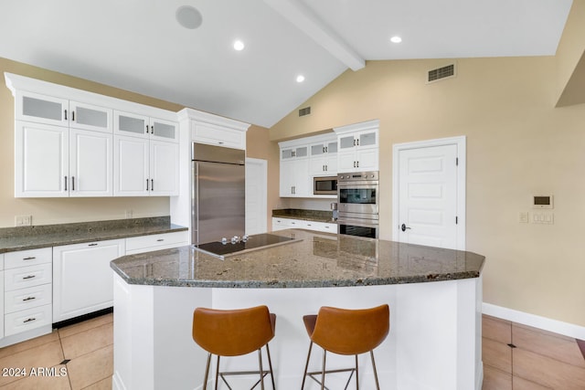 kitchen featuring a center island, vaulted ceiling with beams, built in appliances, dark stone countertops, and white cabinets