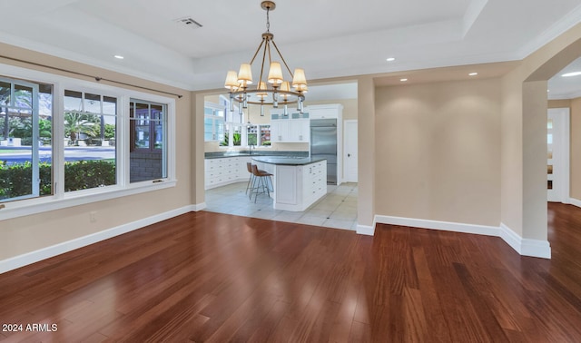 unfurnished dining area with an inviting chandelier, a raised ceiling, sink, and light hardwood / wood-style flooring