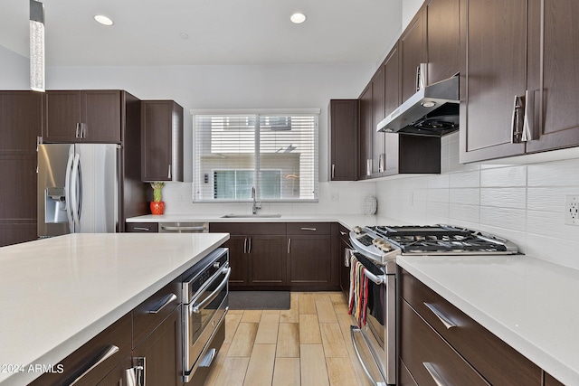 kitchen featuring stainless steel appliances, tasteful backsplash, light countertops, a sink, and wall chimney range hood