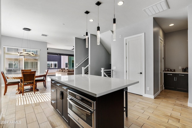 kitchen featuring a kitchen island, visible vents, hanging light fixtures, light countertops, and a kitchen bar