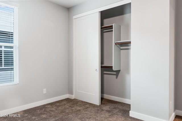 unfurnished bedroom with a closet, dark carpet, and baseboards