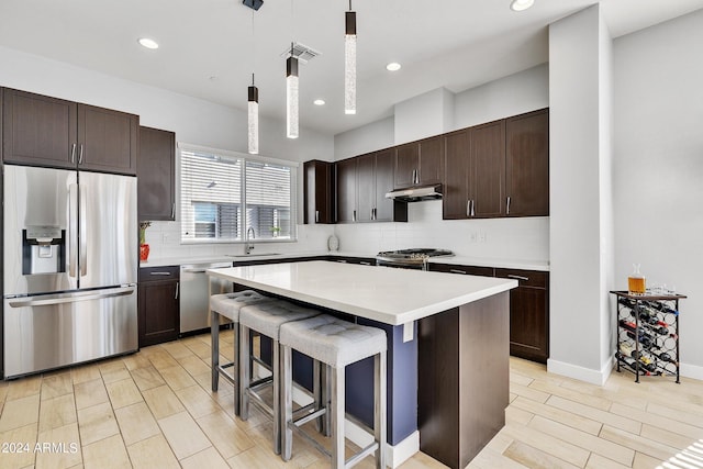 kitchen featuring under cabinet range hood, stainless steel appliances, a sink, light countertops, and decorative light fixtures