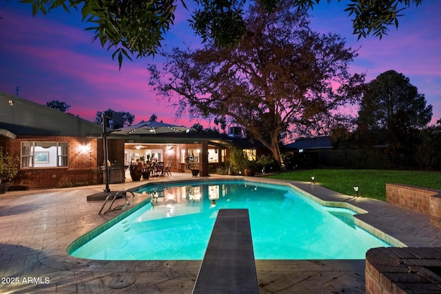 pool at dusk with a patio area and a diving board