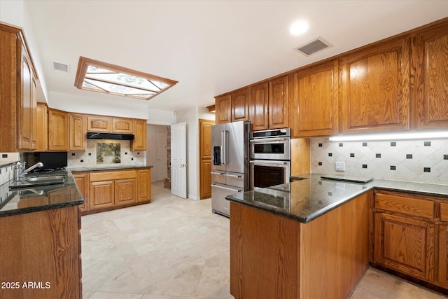 kitchen with sink, tasteful backsplash, appliances with stainless steel finishes, kitchen peninsula, and dark stone counters