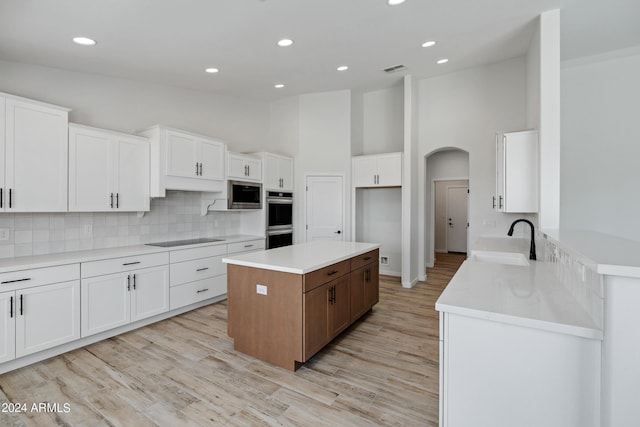 kitchen featuring stainless steel appliances, a kitchen island, a sink, white cabinetry, and decorative backsplash