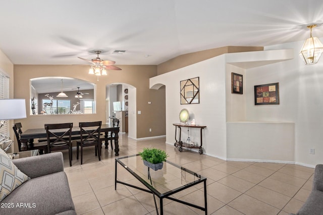 living area featuring arched walkways, ceiling fan, light tile patterned flooring, and baseboards