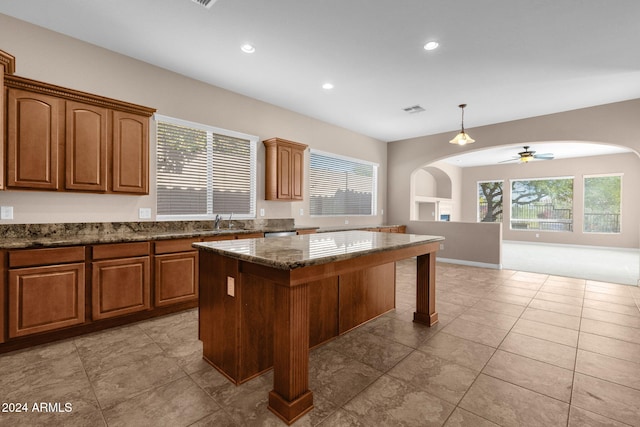 kitchen featuring ceiling fan, sink, dark stone countertops, decorative light fixtures, and a kitchen island