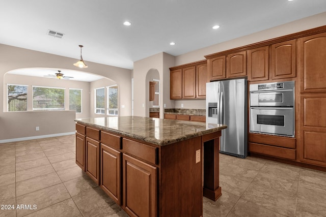 kitchen with pendant lighting, ceiling fan, dark stone countertops, appliances with stainless steel finishes, and a kitchen island