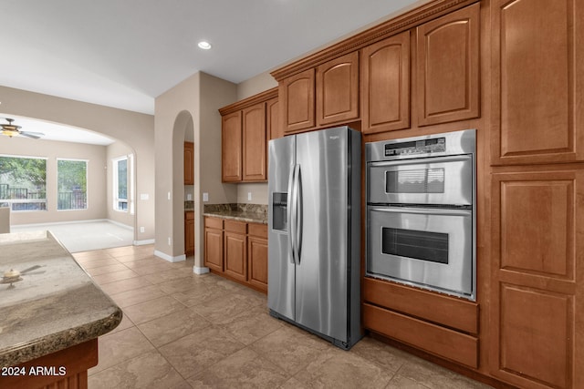 kitchen featuring ceiling fan, light tile patterned floors, stone countertops, and appliances with stainless steel finishes