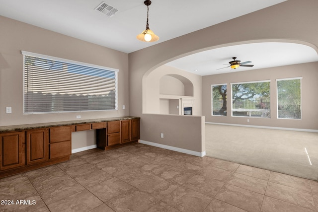 interior space featuring built in shelves, built in desk, light colored carpet, and ceiling fan