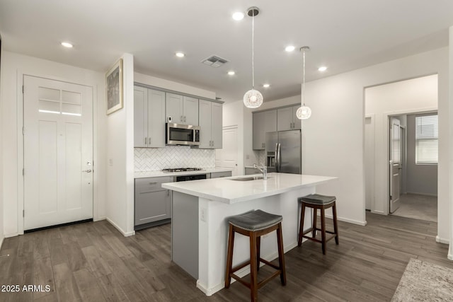 kitchen featuring a kitchen bar, appliances with stainless steel finishes, an island with sink, gray cabinetry, and dark hardwood / wood-style flooring