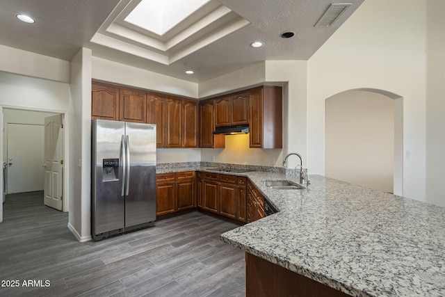 kitchen featuring a sink, under cabinet range hood, stainless steel refrigerator with ice dispenser, visible vents, and arched walkways