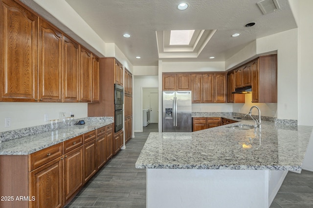 kitchen with stainless steel fridge, under cabinet range hood, a sink, visible vents, and a peninsula