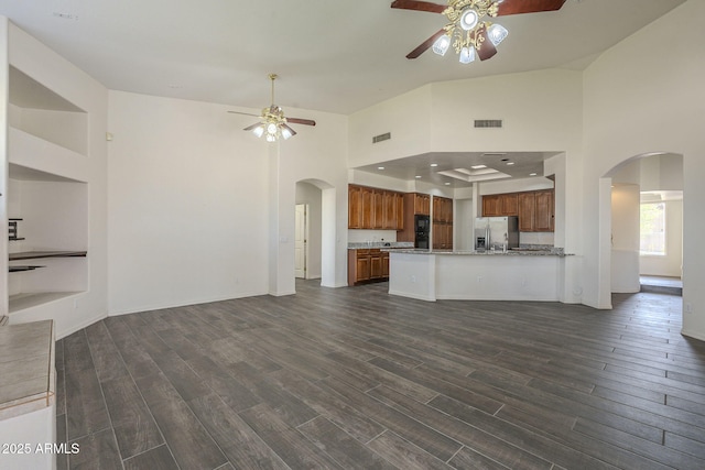 unfurnished living room with dark wood-style flooring, arched walkways, and a ceiling fan