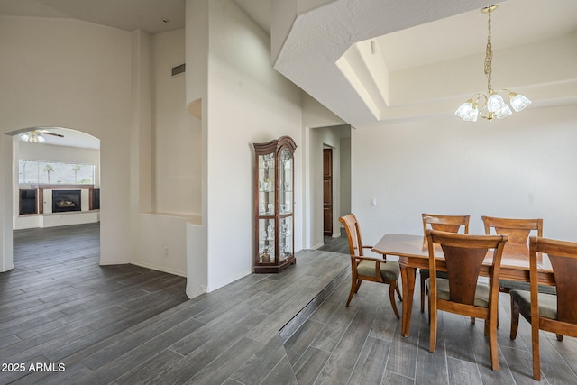 dining room featuring dark wood finished floors, baseboards, ceiling fan with notable chandelier, visible vents, and arched walkways