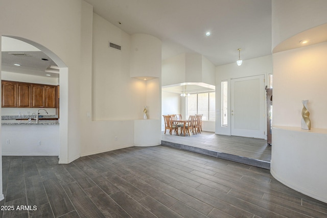 foyer featuring a high ceiling, dark wood-style flooring, arched walkways, and visible vents