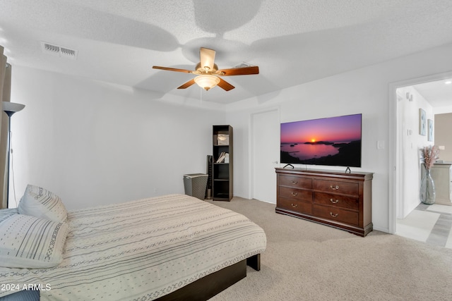 bedroom featuring ceiling fan, light colored carpet, and a textured ceiling