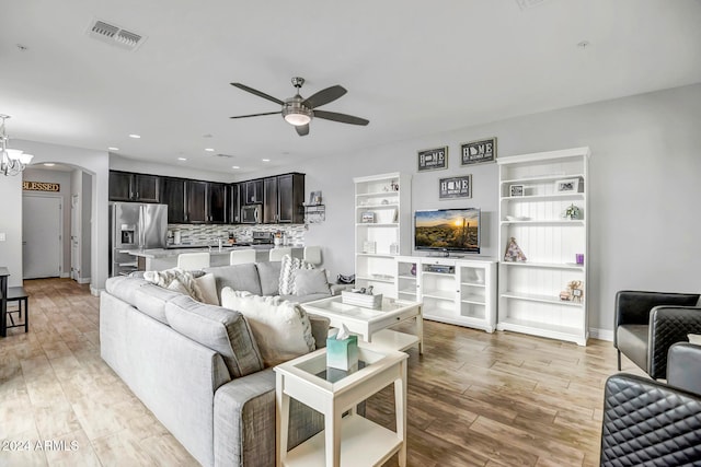 living room with light hardwood / wood-style floors and ceiling fan with notable chandelier