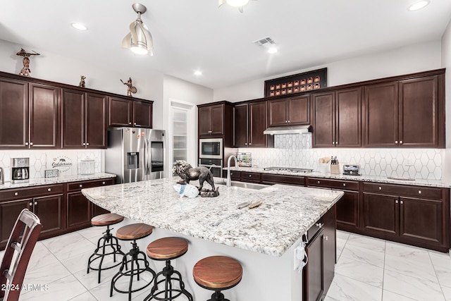 kitchen with light stone counters, a kitchen breakfast bar, stainless steel appliances, backsplash, and a center island with sink