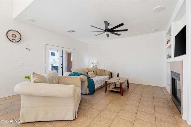 living room featuring ceiling fan, light tile patterned floors, built in features, and a tiled fireplace