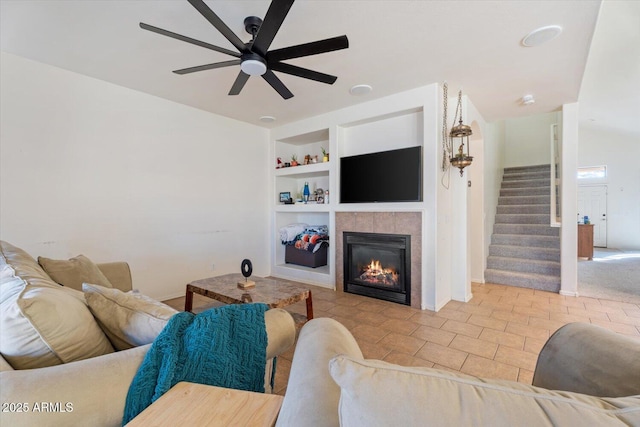 living room featuring ceiling fan, a tiled fireplace, and built in features