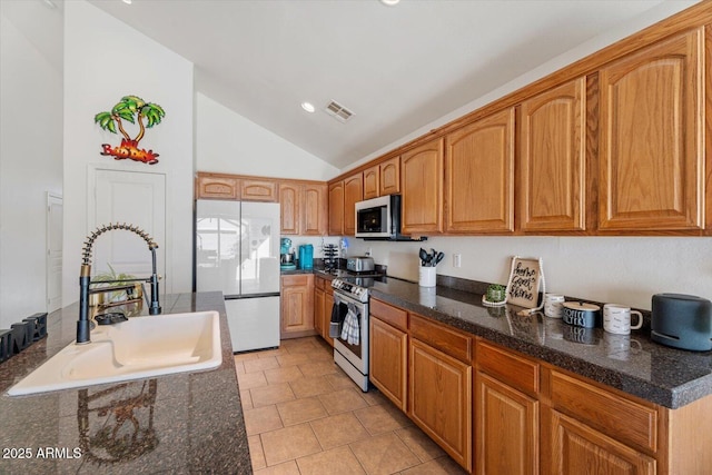 kitchen with lofted ceiling, stainless steel appliances, dark stone counters, sink, and light tile patterned floors