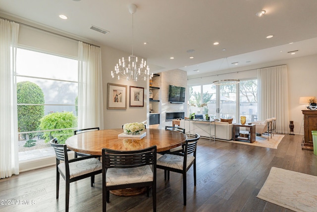 dining space featuring a large fireplace, wood-type flooring, plenty of natural light, and an inviting chandelier