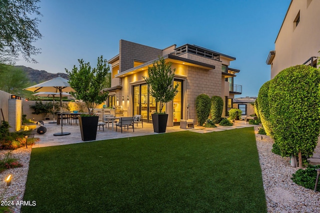 back house at dusk featuring a yard, an outdoor hangout area, a balcony, and a patio area