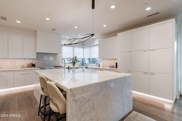 kitchen featuring a center island with sink, dark hardwood / wood-style floors, white cabinetry, and hanging light fixtures