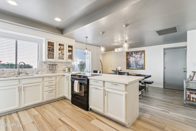 kitchen featuring kitchen peninsula, hanging light fixtures, light hardwood / wood-style floors, electric range, and sink