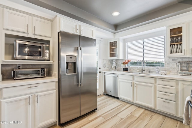 kitchen featuring light hardwood / wood-style floors, stainless steel appliances, decorative backsplash, sink, and white cabinetry