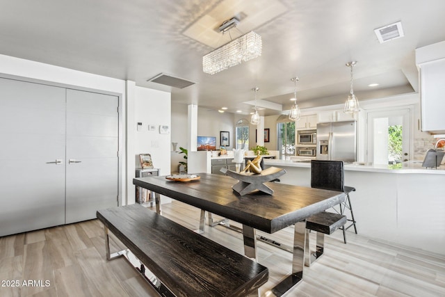 dining room with light wood-type flooring, a tray ceiling, and a chandelier