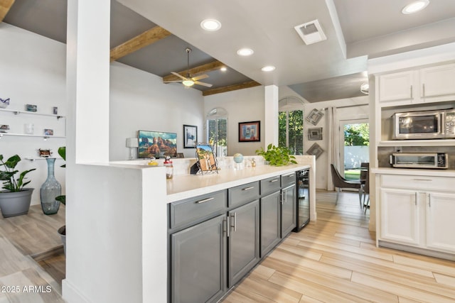 kitchen with beverage cooler, light wood-type flooring, beamed ceiling, ceiling fan, and white cabinets