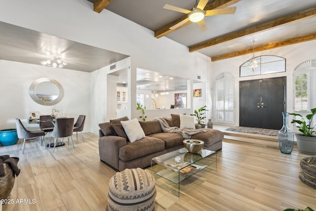 living room featuring light wood-type flooring, ceiling fan with notable chandelier, and beamed ceiling