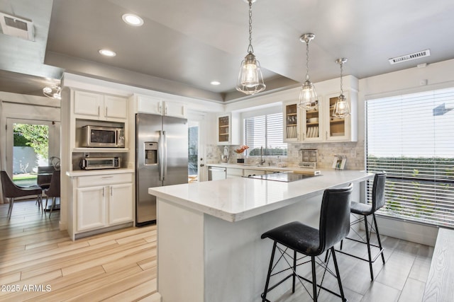 kitchen with hanging light fixtures, stainless steel appliances, plenty of natural light, white cabinetry, and a breakfast bar area