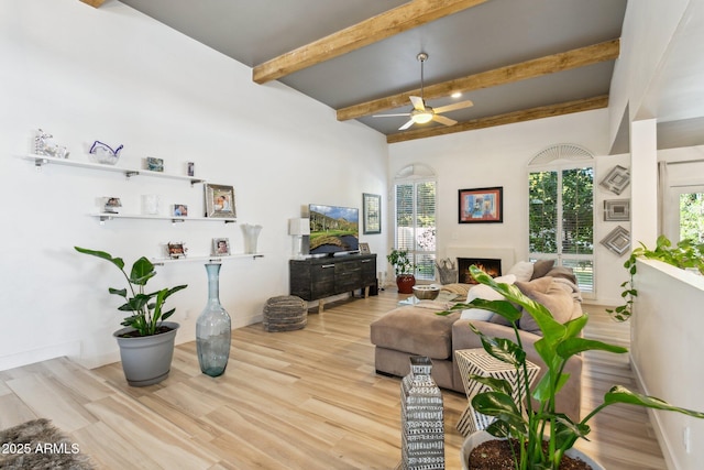 living room with beamed ceiling, ceiling fan, and light wood-type flooring