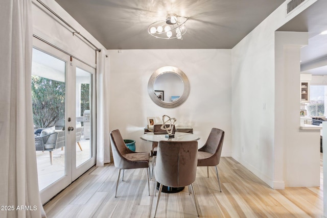 dining space with french doors, a chandelier, light wood-type flooring, and plenty of natural light