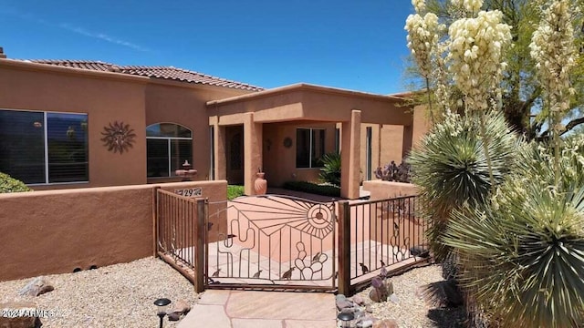 exterior space featuring stucco siding, a tiled roof, fence, and a gate