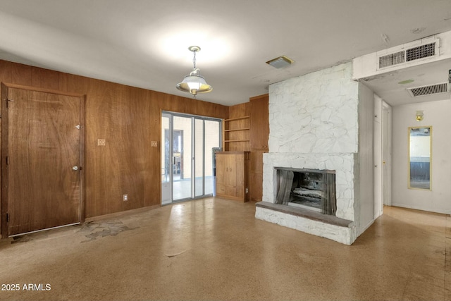 unfurnished living room featuring a stone fireplace, wood walls, and visible vents