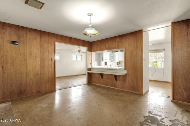 interior space with wooden walls, baseboards, brown cabinets, a kitchen breakfast bar, and hanging light fixtures