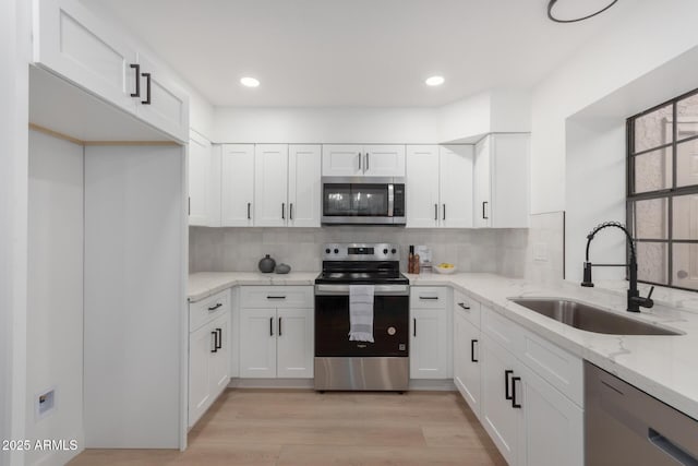 kitchen with sink, white cabinetry, stainless steel appliances, light stone countertops, and light wood-type flooring