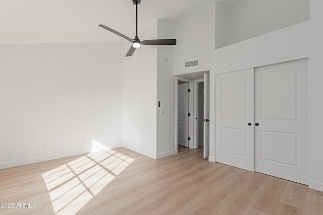 unfurnished bedroom with a high ceiling, ceiling fan, light wood-type flooring, and a closet