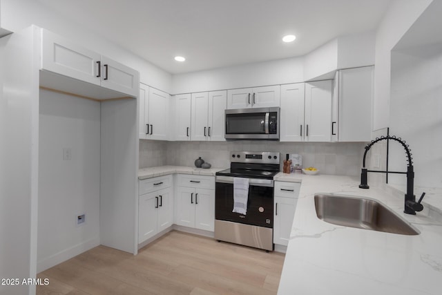 kitchen with appliances with stainless steel finishes, white cabinetry, sink, light hardwood / wood-style floors, and light stone countertops