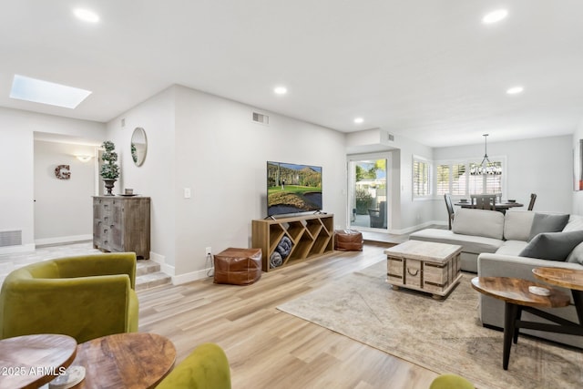 living room featuring a skylight, light hardwood / wood-style floors, and an inviting chandelier