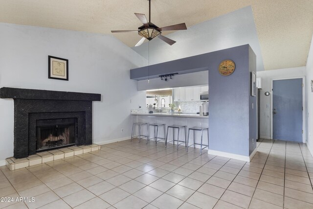 tiled living room with high vaulted ceiling, ceiling fan, and a tile fireplace