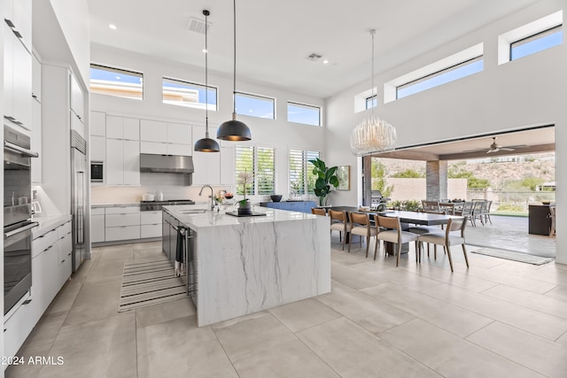 kitchen with white cabinets, backsplash, an island with sink, a high ceiling, and pendant lighting