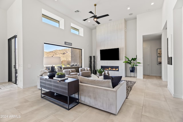 living room with light tile patterned floors, a high ceiling, a large fireplace, and ceiling fan