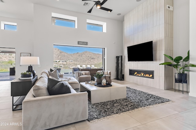 living room with a towering ceiling, a tiled fireplace, light tile patterned flooring, and plenty of natural light